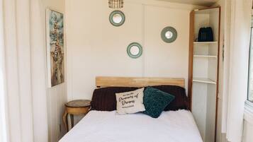 A bedroom with a bed, a nightstand, a shelf, and a hanging light fixture.