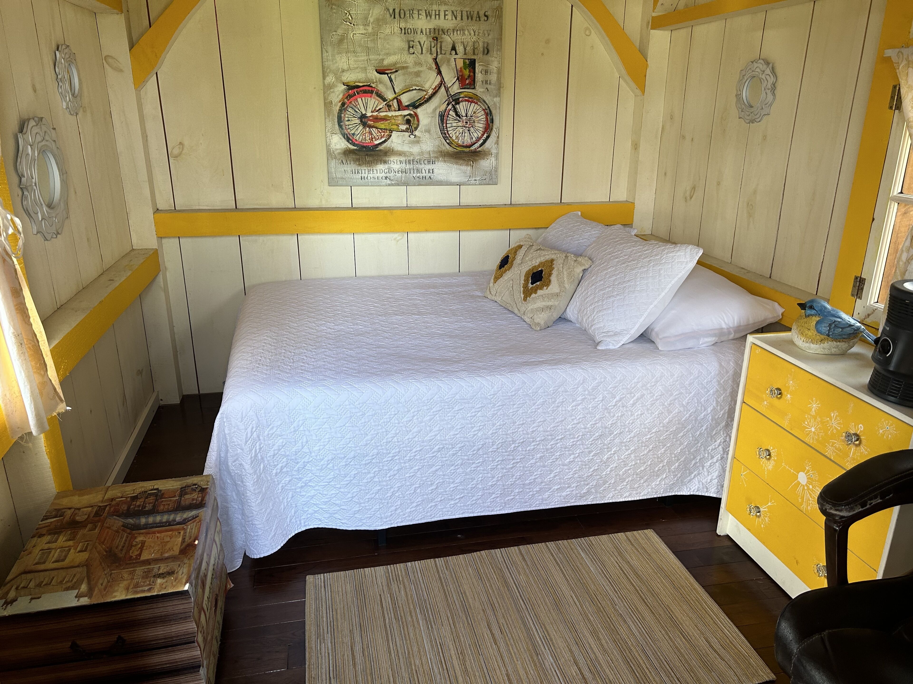 A bedroom with a bed, a yellow dresser, a chair, and a poster on the wall.