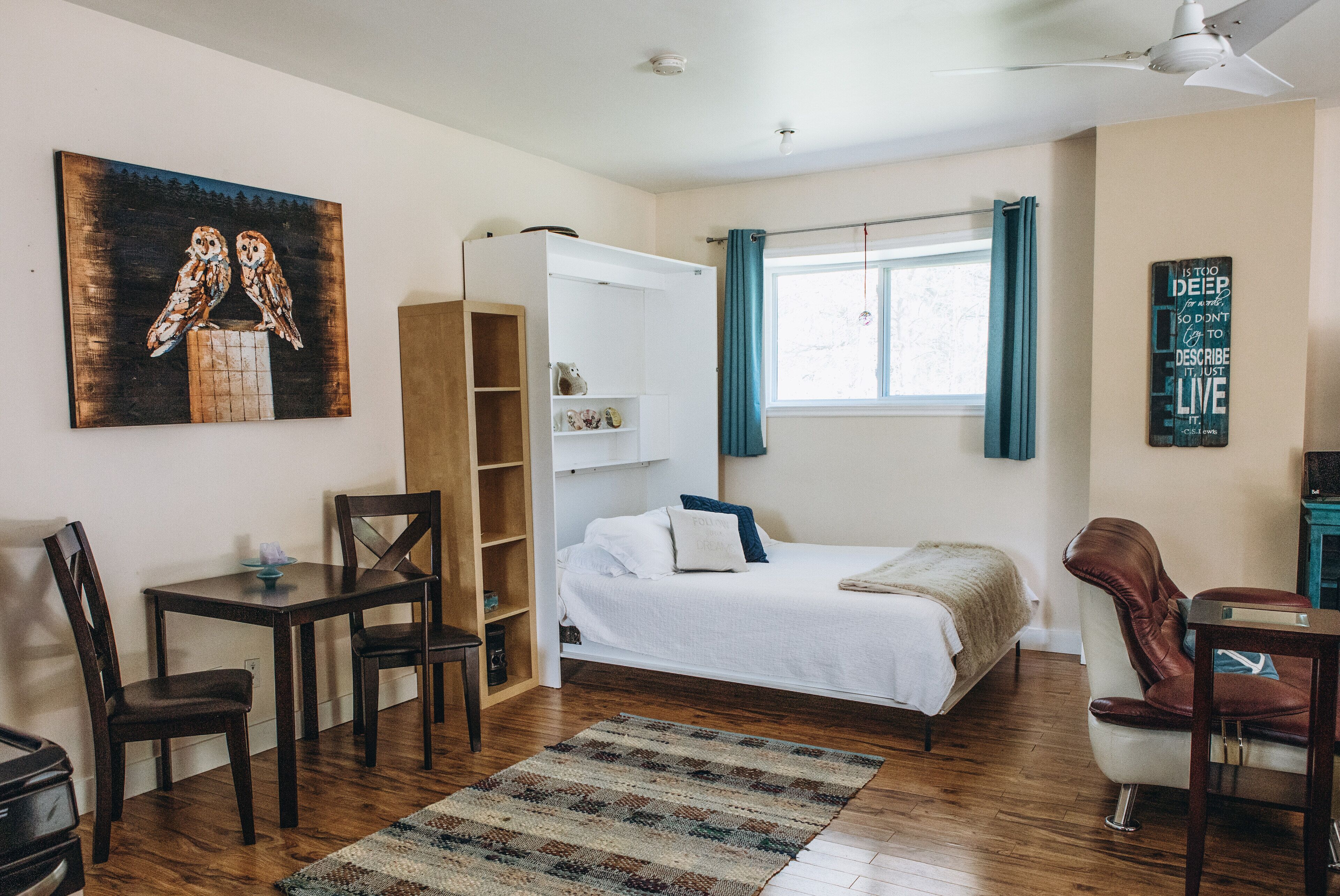 A bedroom with a bed, a desk, chairs, a wardrobe, and a painting of owls.