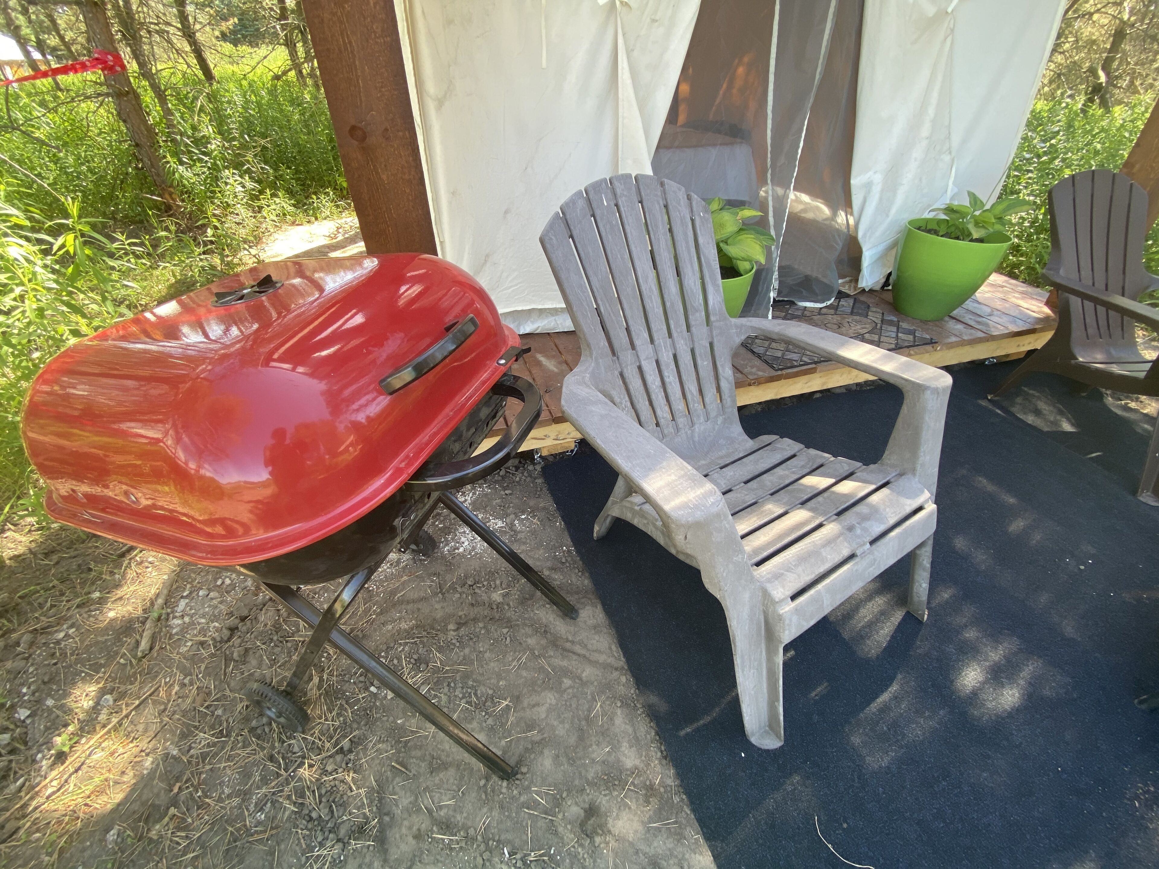 A red grill and two Adirondack chairs in an outdoor setting.
