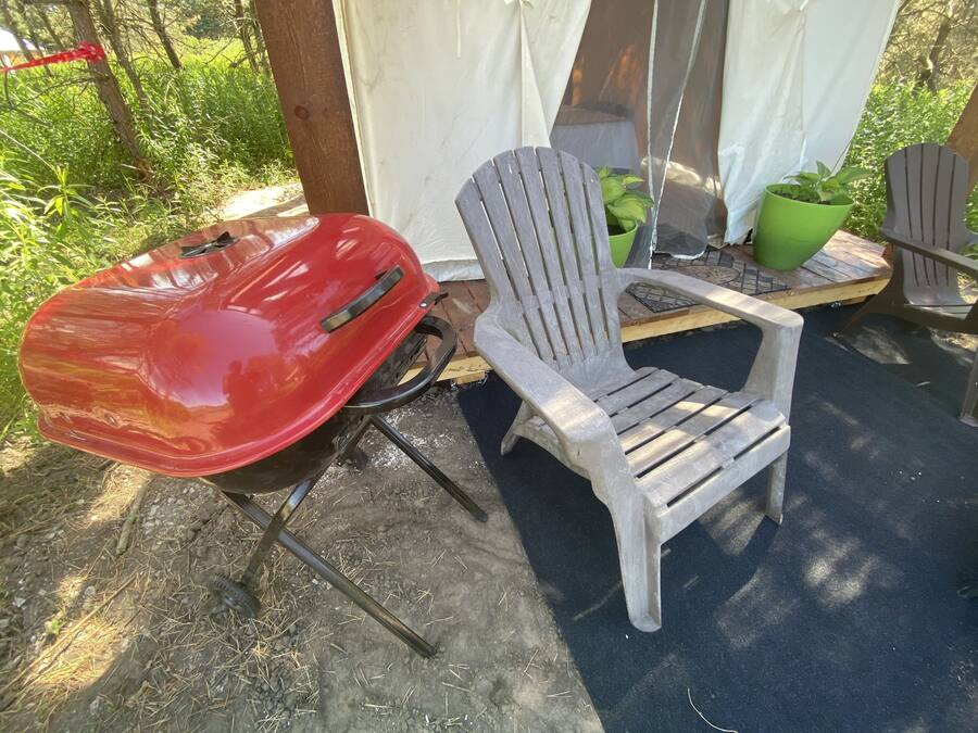 A red grill and two Adirondack chairs in an outdoor setting.