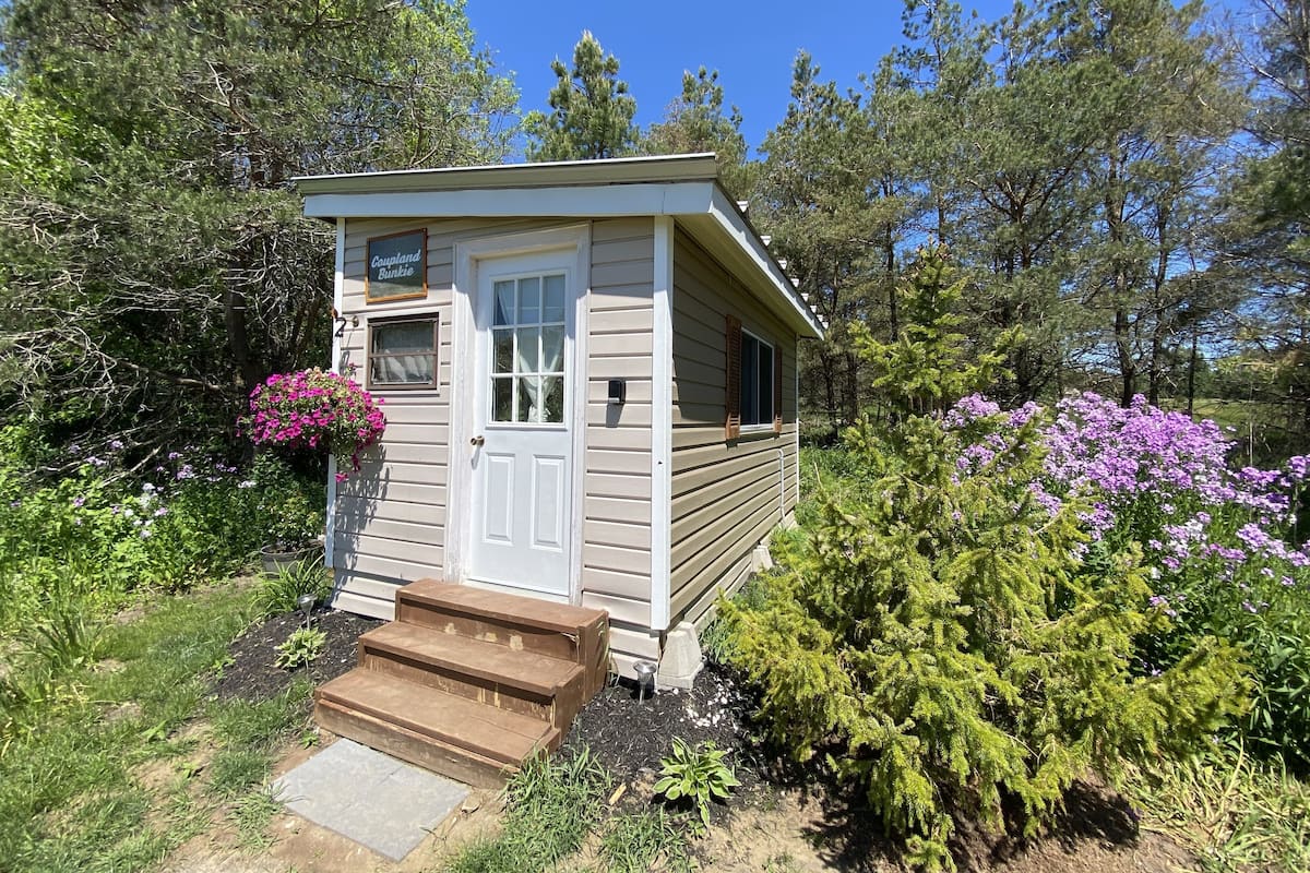 A small wooden cabin with a white door, a window, and a sign that reads "Coupland Bunkie."