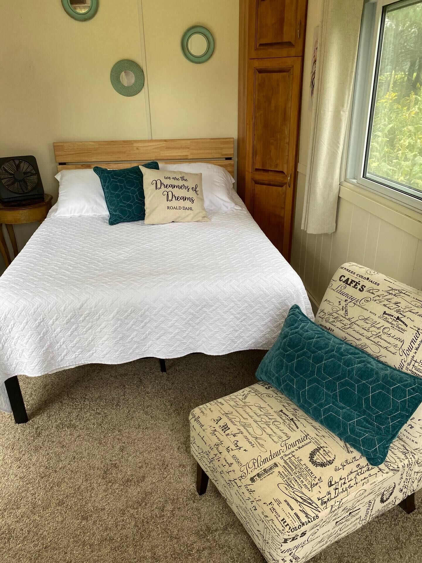 A bedroom with a bed, a nightstand, a wooden wardrobe, and a window with curtains.