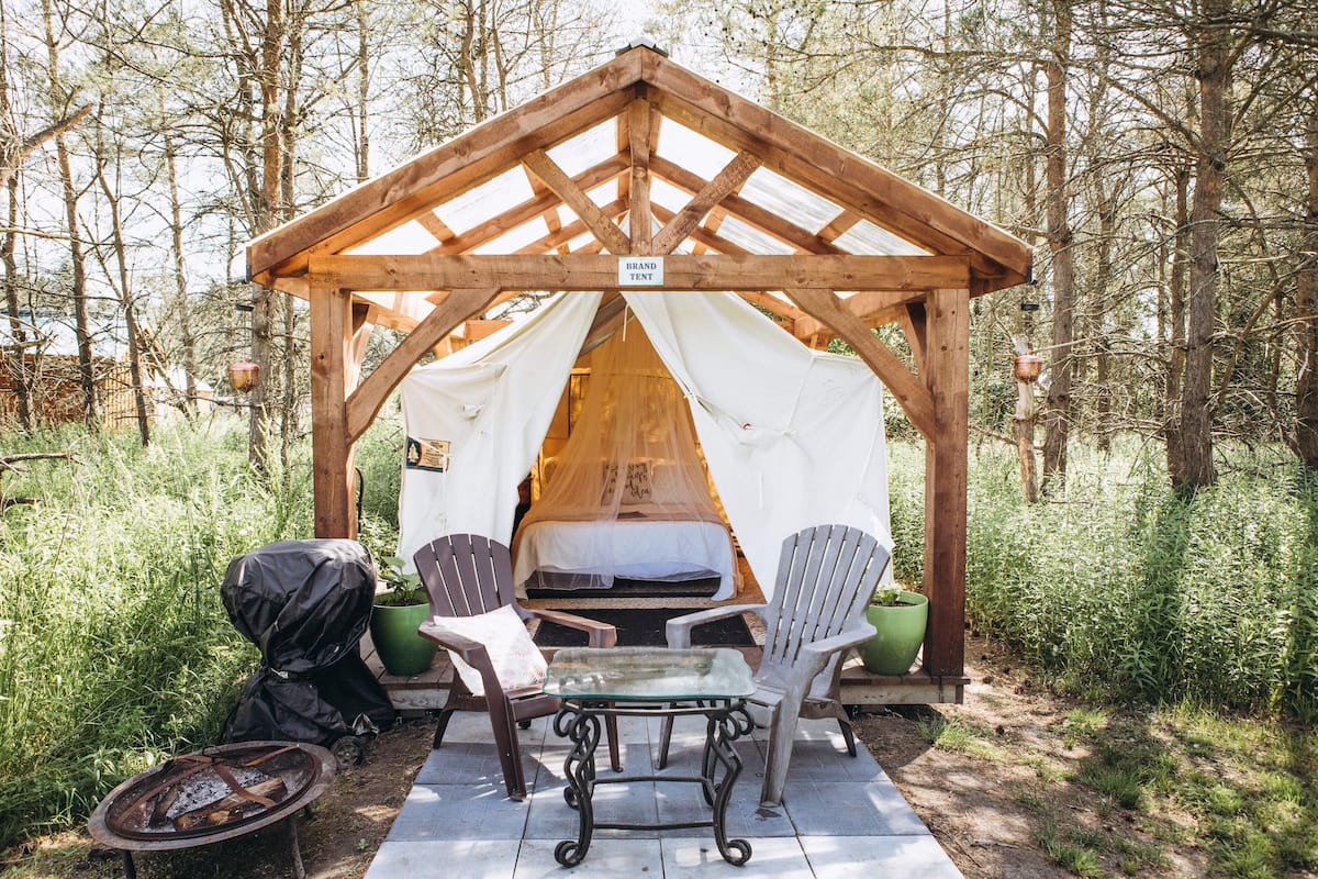 A wooden tent with a canopy, a table, two chairs, and a grill.