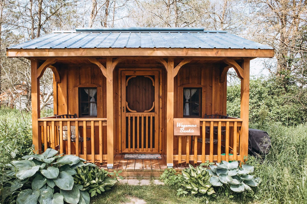 A wooden cabin with a metal roof, a front porch, and a sign reading "Wegmans Bunkie".