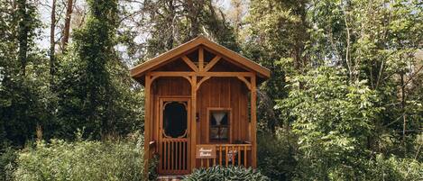 A wooden cabin with a porch, surrounded by dense forest.