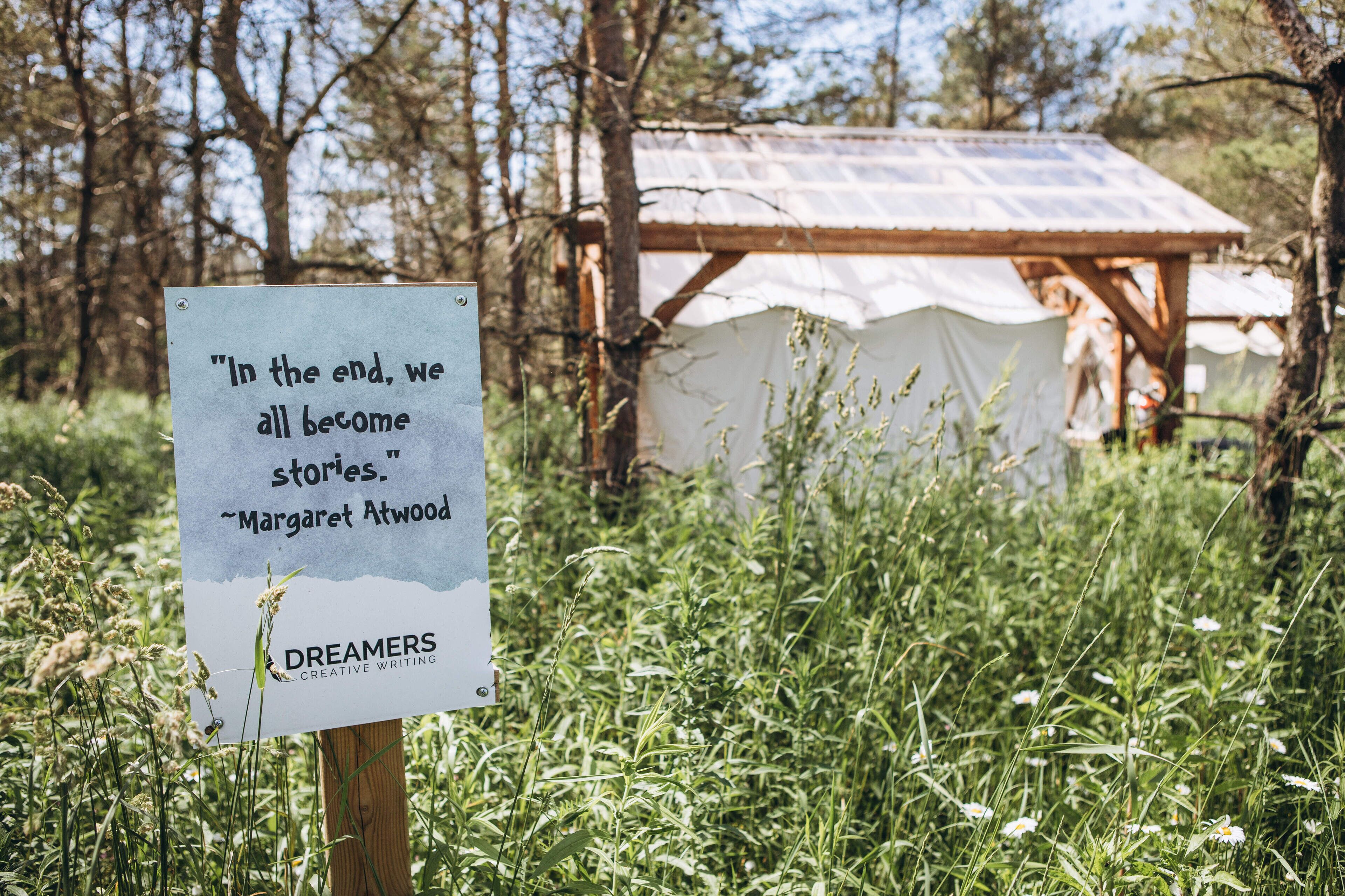 A sign with a quote in a natural setting with a wooden structure in the background.
