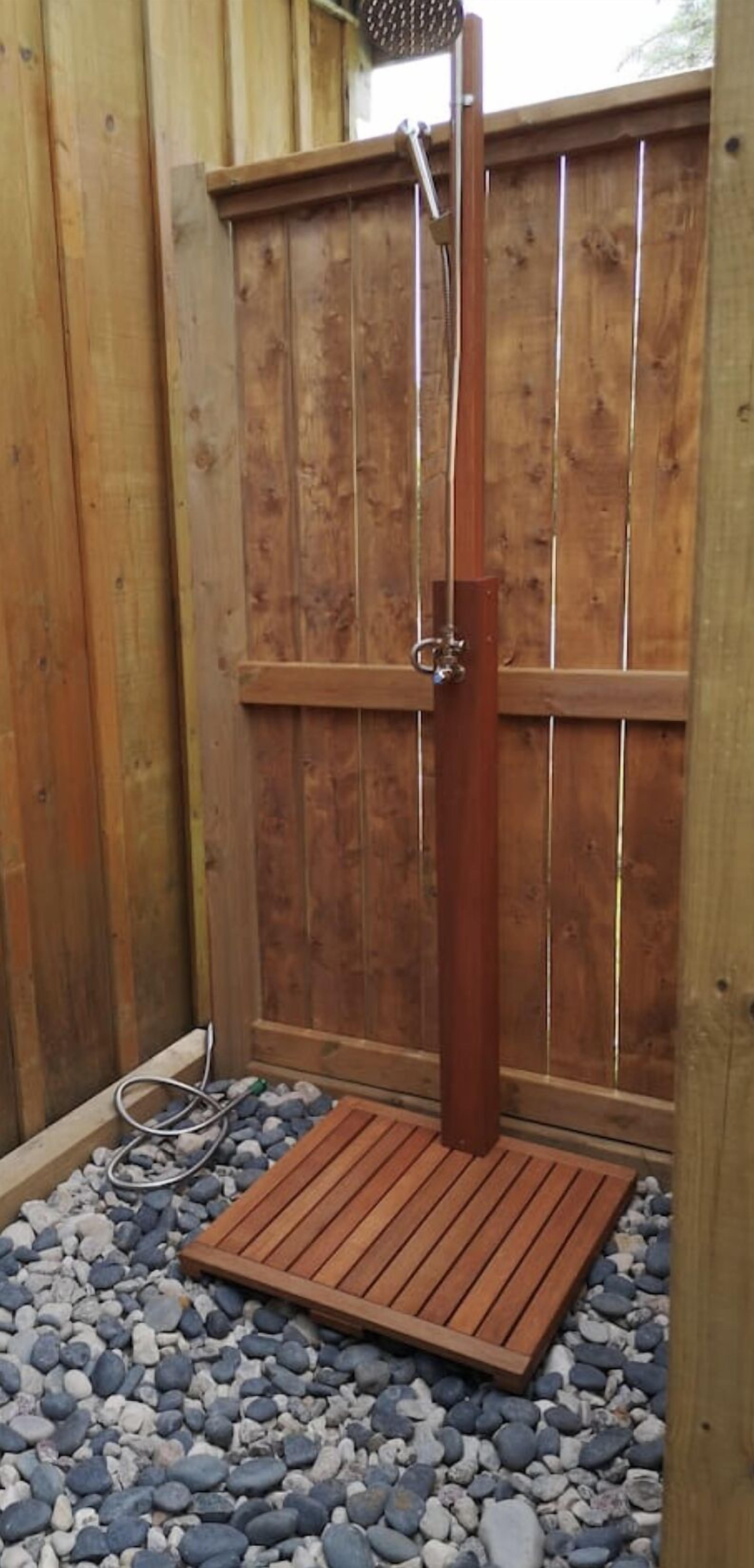A wooden shower enclosure with a metal showerhead and a wooden platform.