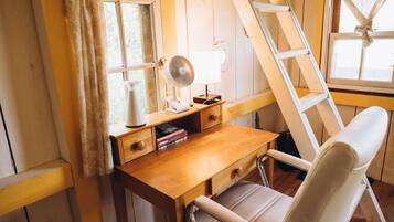 A wooden desk with a white chair, a standing fan, and a window with curtains.
