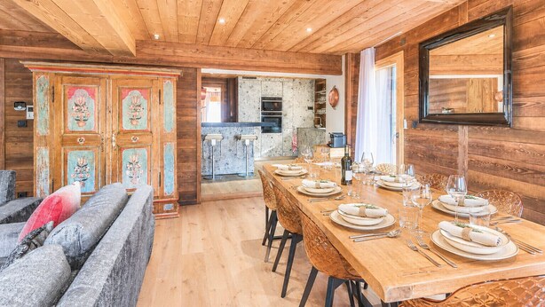 A wooden interior with a dining area set for a meal, a kitchen in the background, and a large mirror on the wall.