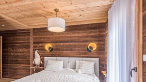 A cozy wooden cabin bedroom with a bed, pillows, a fluffy white blanket, and a hanging light fixture.
