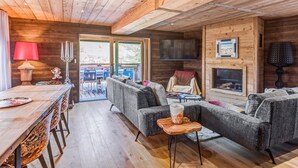 A cozy cabin interior with a wooden ceiling, a dining area with a table and chairs, a fireplace, and a sofa set.