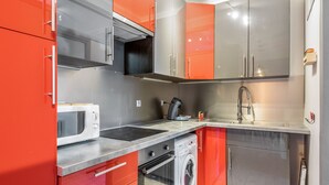 Una cocina compacta con electrodomésticos de acero inoxidable, armarios rojos y un microondas.