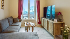 Una sala de estar con sofá, una mesa de centro, un televisor sobre un mueble de madera y una ventana con cortinas.