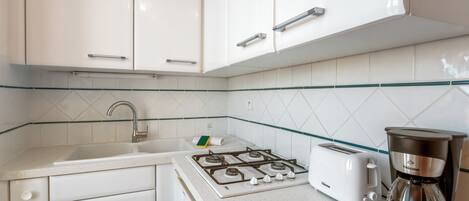 Una cocina con armarios blancos, estufa a gas, tostadora y cafetera.