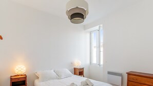 Un dormitorio con cama, lámparas de noche, cómoda y ventana.