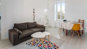 Una sala de estar moderna con un sofá marrón, sillas blancas, una mesita redonda y un tapete colorido.