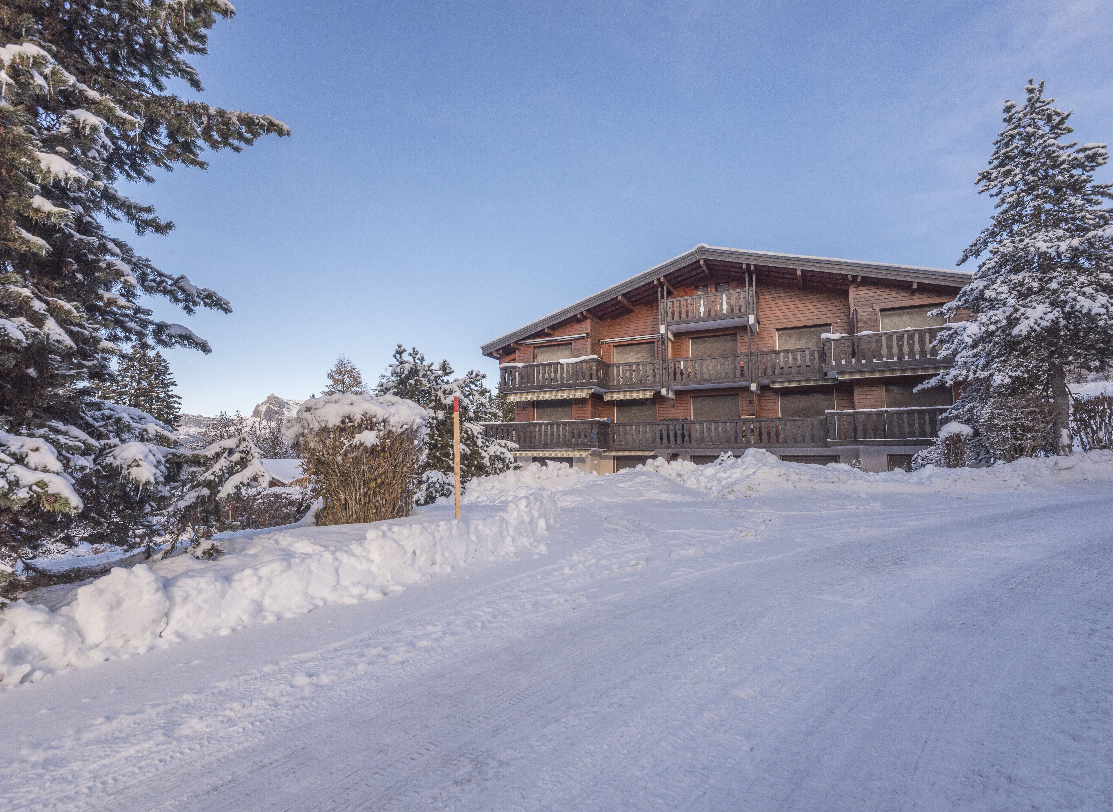 Ein mehrgeschossiges Gebäude mit Balkonen, umgeben von schneebedeckten Bäumen und wolkenlosem Himmel.