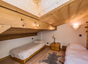 Ein Schlafzimmer mit zwei Betten, Holzbalkendecke, Zebra-Teppich und einem Nachttisch mit Lampe.