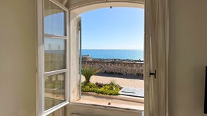 A window with a view of a beach and a stone wall. - Appartement Portolan - Welkeys (Antibes)