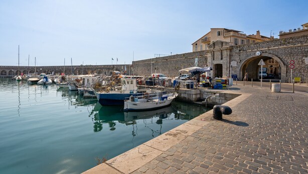 A harbor with boats docked, a stone wall, and a paved walkway. - Appartement Portolan - Welkeys (Antibes)