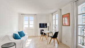 A bright, white room with a bed, a TV, a small table, and chairs. - Appartement Portolan - Welkeys (Antibes)