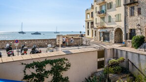 A coastal building with a stone facade, a balcony with plants, and a view of the sea with boats. - Appartement Portolan - Welkeys (Antibes)