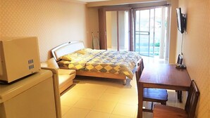 A hotel room with a bed, a desk, a chair, a television, and a window with curtains. - Jomtien Beach Studio Condo - Sleeps 2 - near Beach (Muang Pattaya)