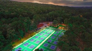 An aerial view of a tennis court complex surrounded by dense forest. - Beautiful, Large Lake House, Made for Family Fun! (Hot Springs Village)
