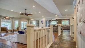 A spacious living area with a high ceiling, a ceiling fan, and a kitchen area with a stone floor. - Beautiful, Large Lake House, Made for Family Fun! (Hot Springs Village)