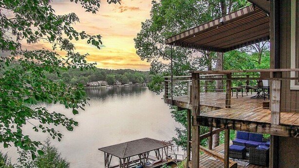 A wooden deck with outdoor seating and a view of a lake at sunset. - Beautiful, Large Lake House, Made for Family Fun! (Hot Springs Village)