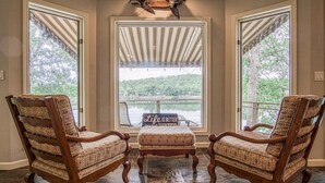 A room with three wooden chairs and a bench, a large window with a view of a lake, and a mounted animal head on the wall. - Beautiful, Large Lake House, Made for Family Fun! (Hot Springs Village)