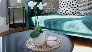 A modern living room with a teal sofa, a glass coffee table with a plant, and a framed artwork on the wall. - 1 Bed Loft - Sleeps 2 - Parking - Wifi (Newport)