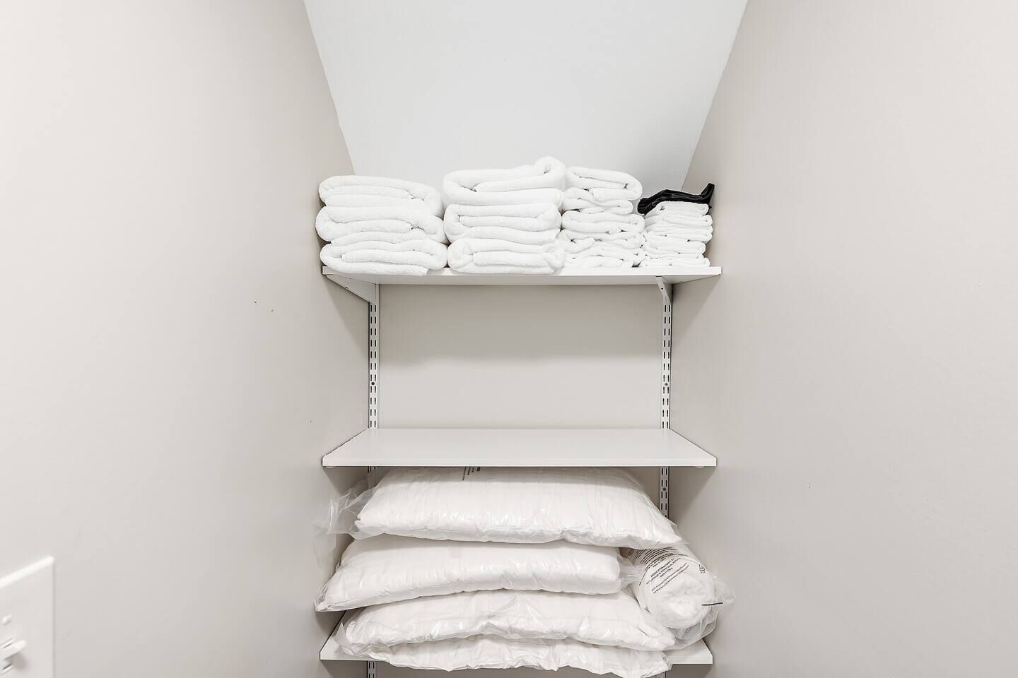 A storage area with shelves holding folded towels and a stack of pillows.