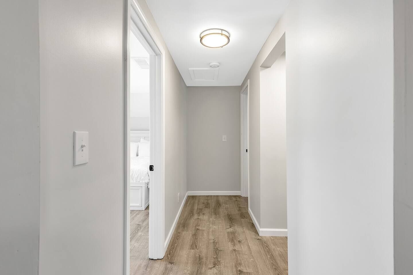 Ein schmaler Flur mit weißen Wänden und Holzdielen, der zu einem Schlafzimmer mit Bett und einer weißen Tür führt.