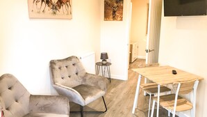 Un salon comprenant un canapé, une table et des chaises, une horloge et des œuvres d’art accrochées au mur.