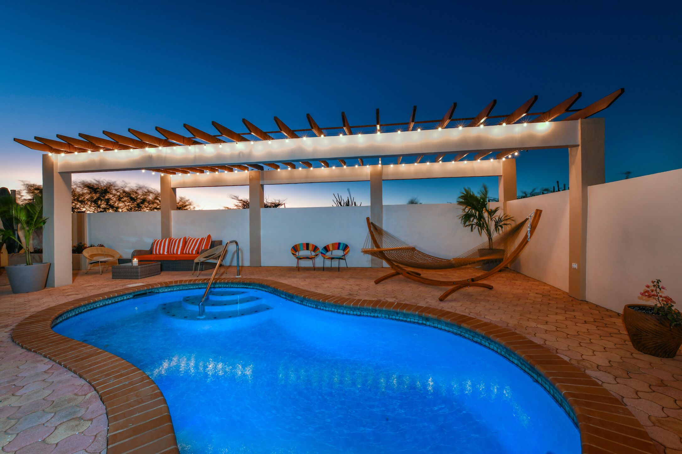 Piscina con una pérgola, rodeada de sillas de descanso y una hamaca.