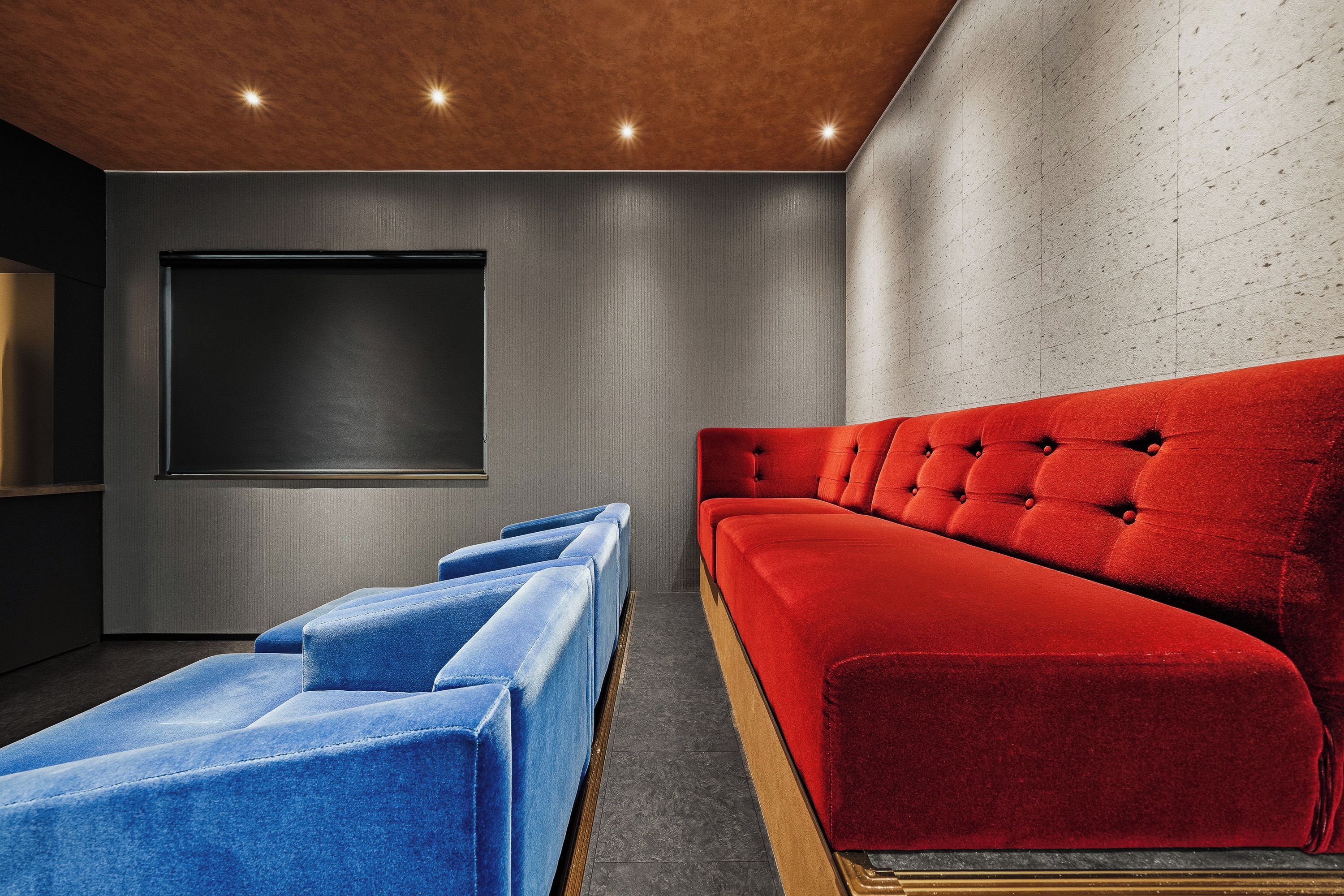 Een moderne bioscoopzaal met een rode bank, blauwe fauteuils en een groot scherm.