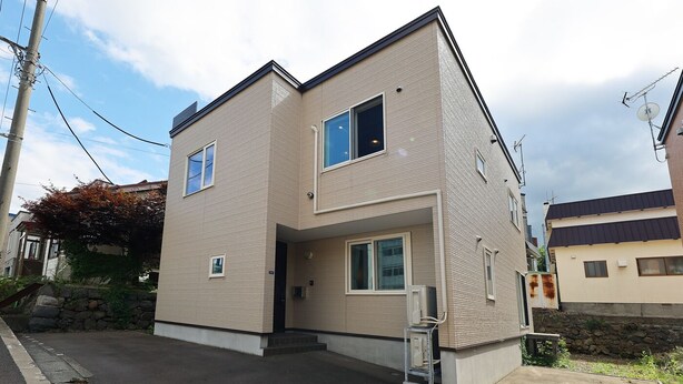 A two-story residential building with a flat roof, a small front porch, and a visible satellite dish. - The Beehive Otaru (Otaru)