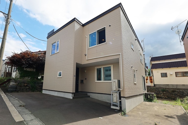 A two-story residential building with a flat roof, a small front porch, and a visible satellite dish. - The Beehive Otaru (Otaru)