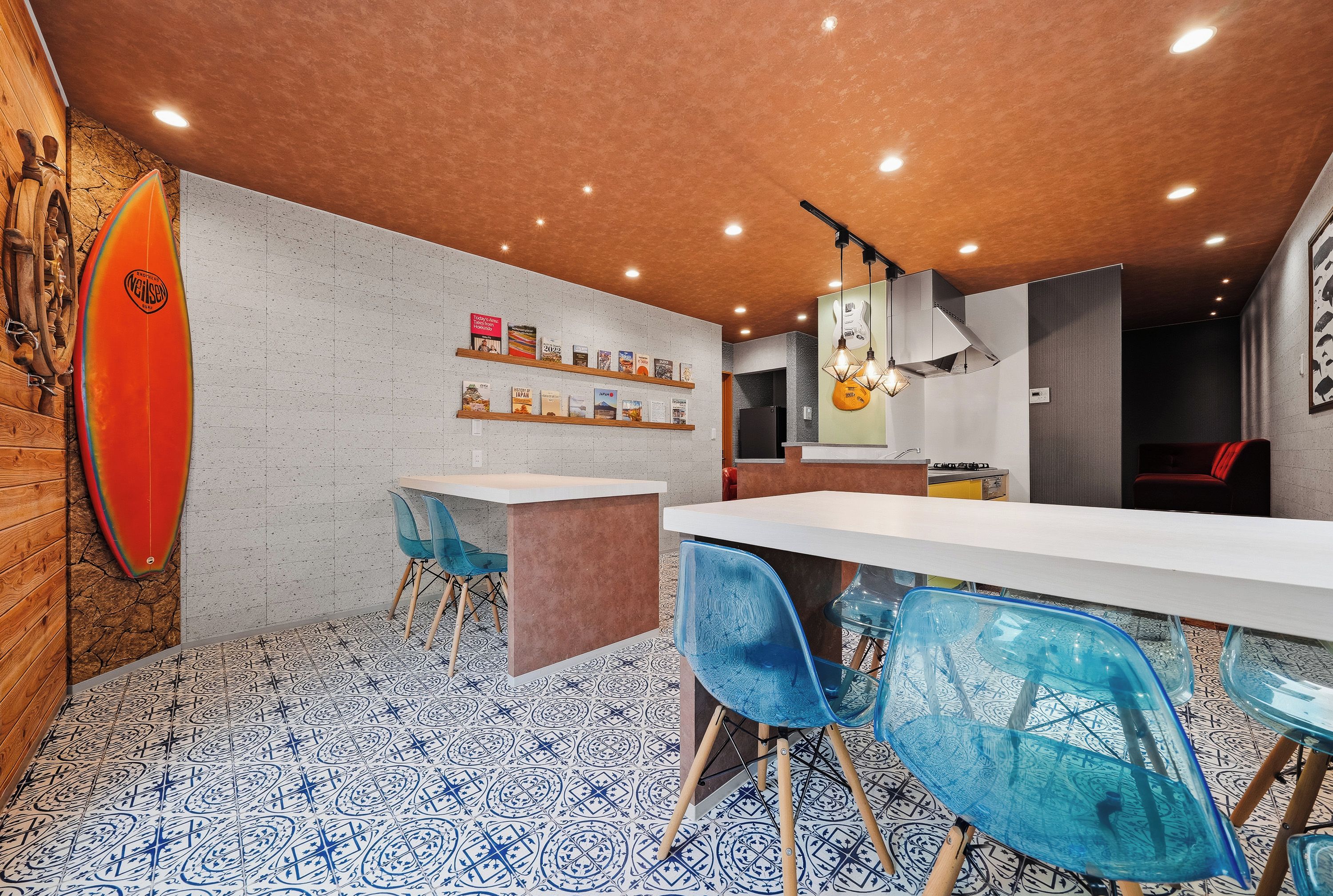Een moderne eetruimte met een witte tafel, blauwe stoelen en een surfboard aan de muur.