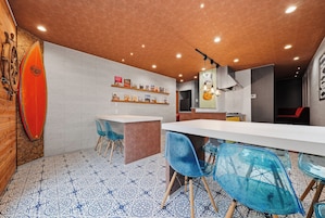 A modern dining area with a white table, blue chairs, and a surfboard on the wall.