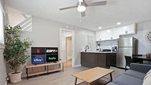 Una sala de estar moderna con televisor mostrando servicios de transmisión, comedor y cocina con refrigerador.