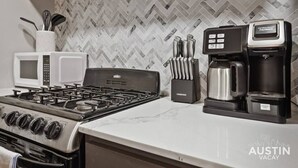 Una cocina con estufa a gas, dos microondas blancos, una cafetera y un juego de cuchillos.