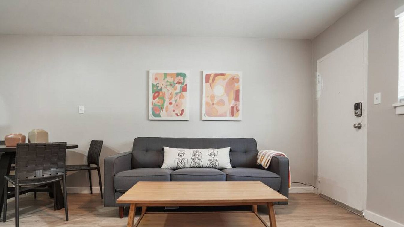 A living room with a grey sofa, a wooden coffee table, and two abstract paintings on the wall.