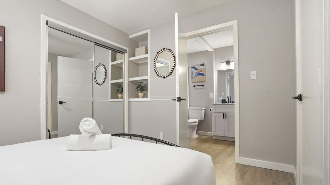 Un dormitorio con cama, un baño con inodoro y lavamanos, y un pasillo que lleva a un armario.