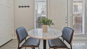 A dining area with a round marble table, two black upholstered chairs, a potted plant, and a door with a coat rack. - Explore Austin Life, Studio Near Guadalupe St (Austin)