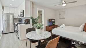 A compact hotel room with a kitchenette, a bed, a dining area, and a TV displaying streaming services. - Explore Austin Life, Studio Near Guadalupe St (Austin)