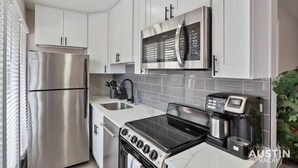 A modern kitchen with stainless steel appliances, white cabinetry, and a black stovetop. - Explore Austin Life, Studio Near Guadalupe St (Austin)