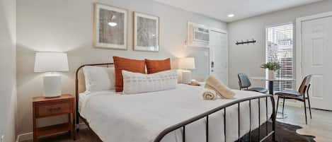 Une chambre à coucher avec un lit, des tables de chevet, une lampe, une chaise et une fenêtre avec des stores.